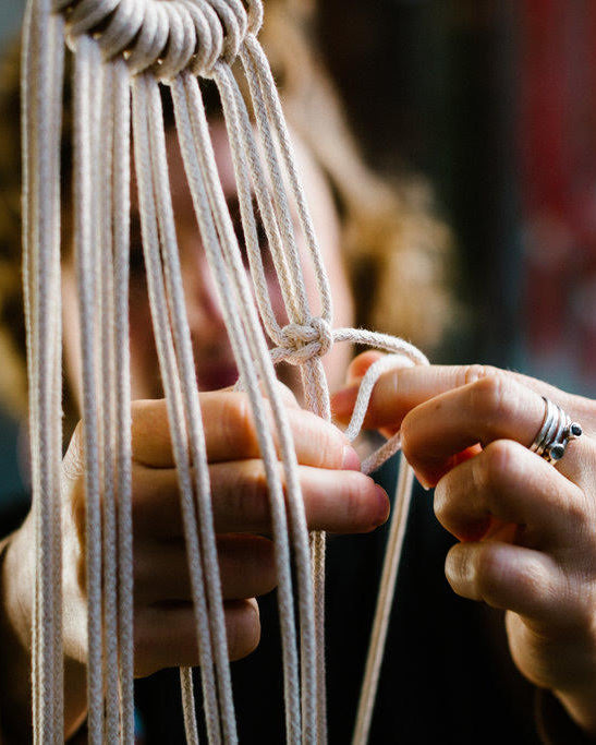 A woman's hand tying knots with hanging cords.