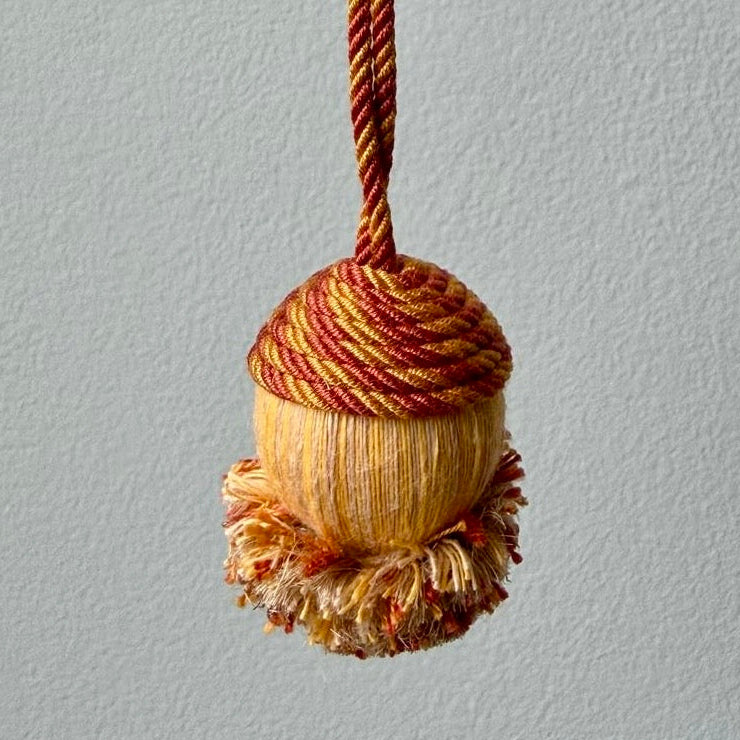 Decorative passementerie tassel with rust and yellow gold colors on a light blue background