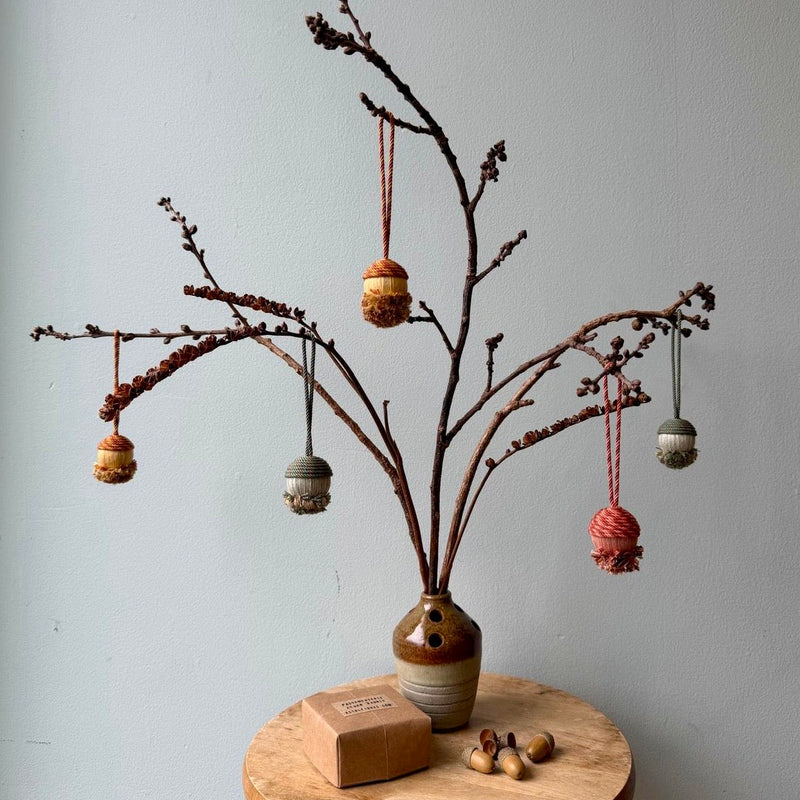 Colourful passementerie ornaments hanging from branches in a rustic brown vase