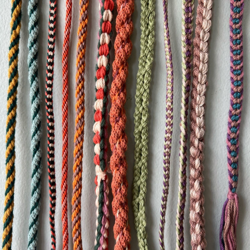 Collection of colourful Kumihimo braided cords on a light blue background