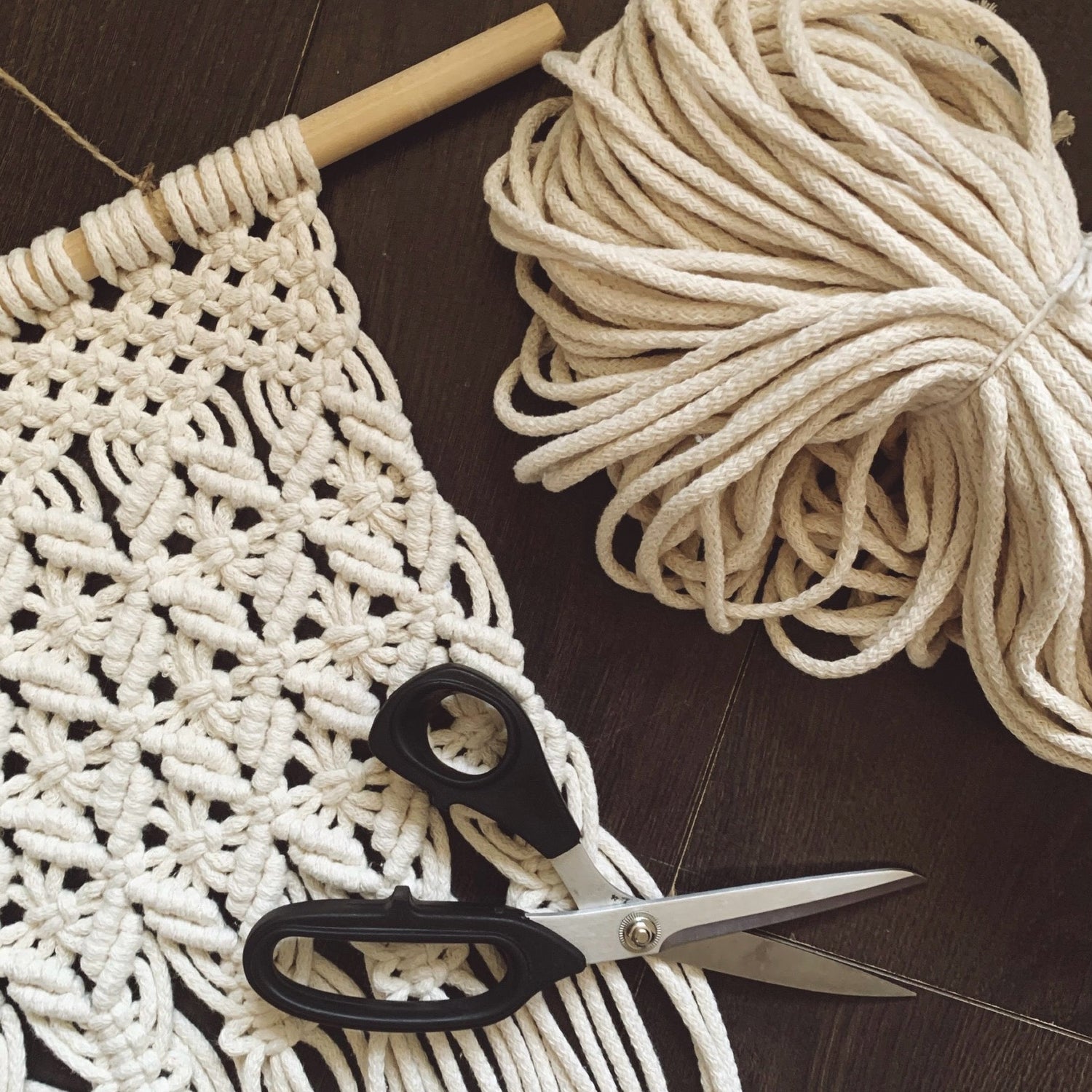 A pair of scissors, a bundle of cord and a macrame wall hanging placed on a ark surface