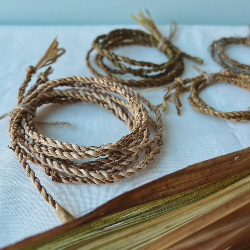 3 coils of handmade cordage placed on a table beside the raw plant fi  res the cord was made with.
