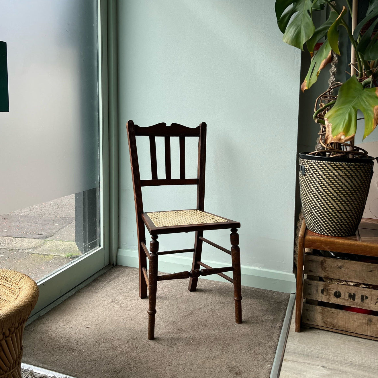 Wooden chair with woven seat cane in a room with a light blue wall and a plant.