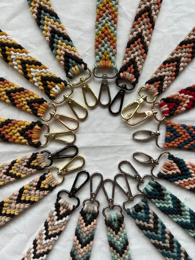 A selection of colourful and patterned macrame key charms placed in a circle on a white background