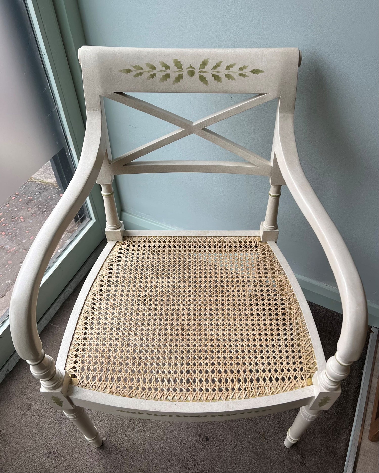 Decorative painted Clive Christian dining chair with 6 way woven cane seat against a light blue wall.