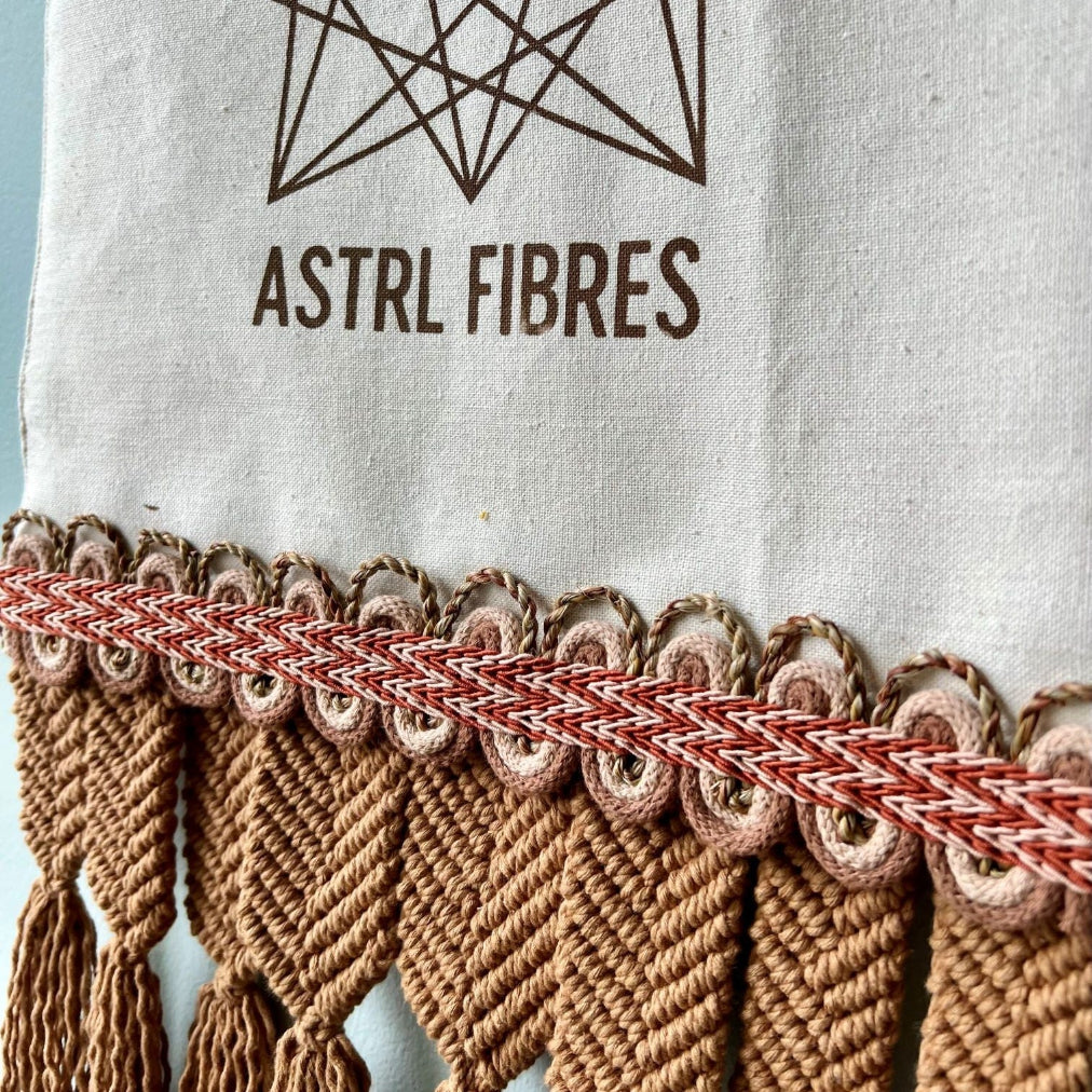 Banner with ASTRL Fibres branding on an off white background with macramé, ply-split braiding and handmade plant cordage embellishments in rust, blush and brown. 
