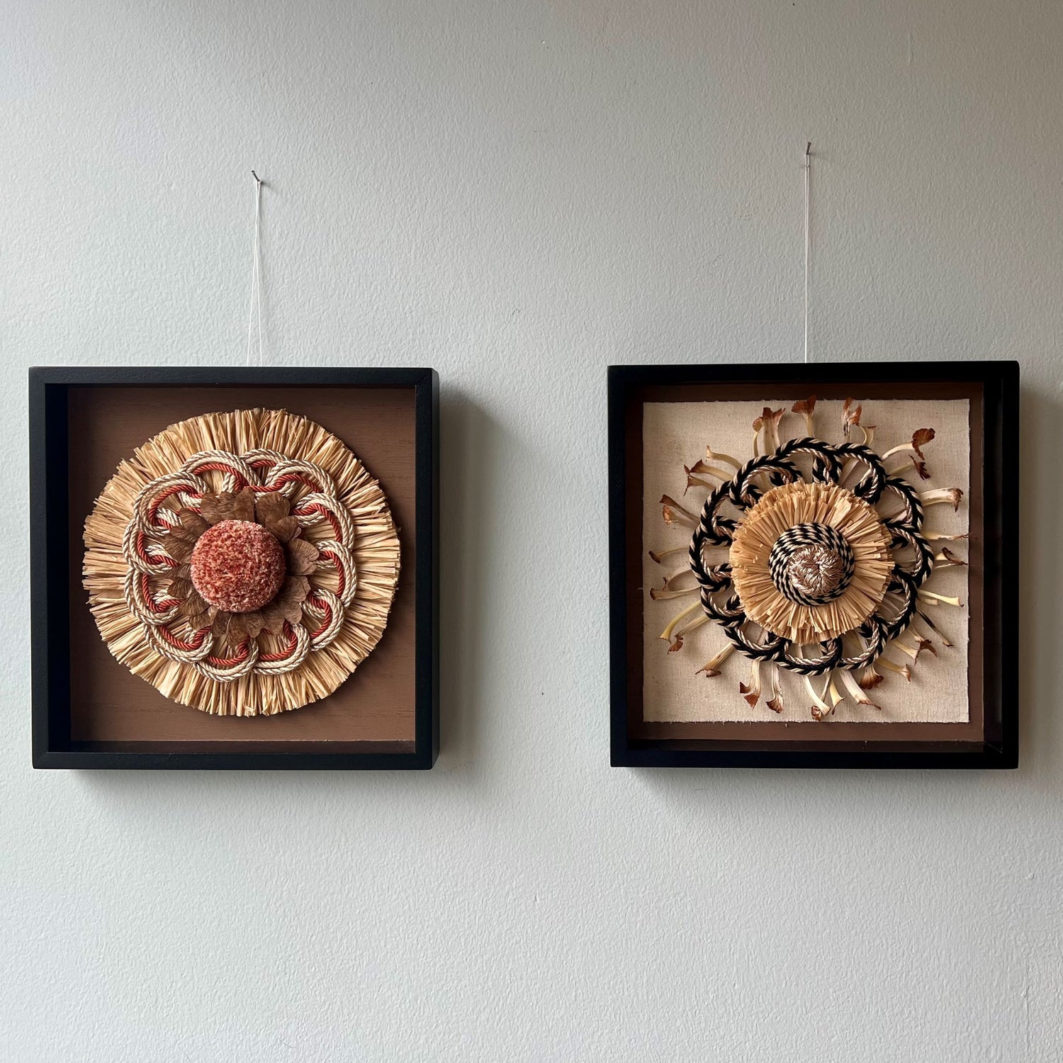 2 colourful framed passementerie rosettes of natural materials and hung on a light blue wall