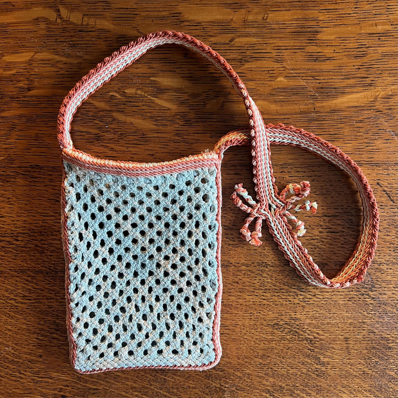 Small light blue bag with multicoloured strap in ply-split braiding design with on a wood surface
