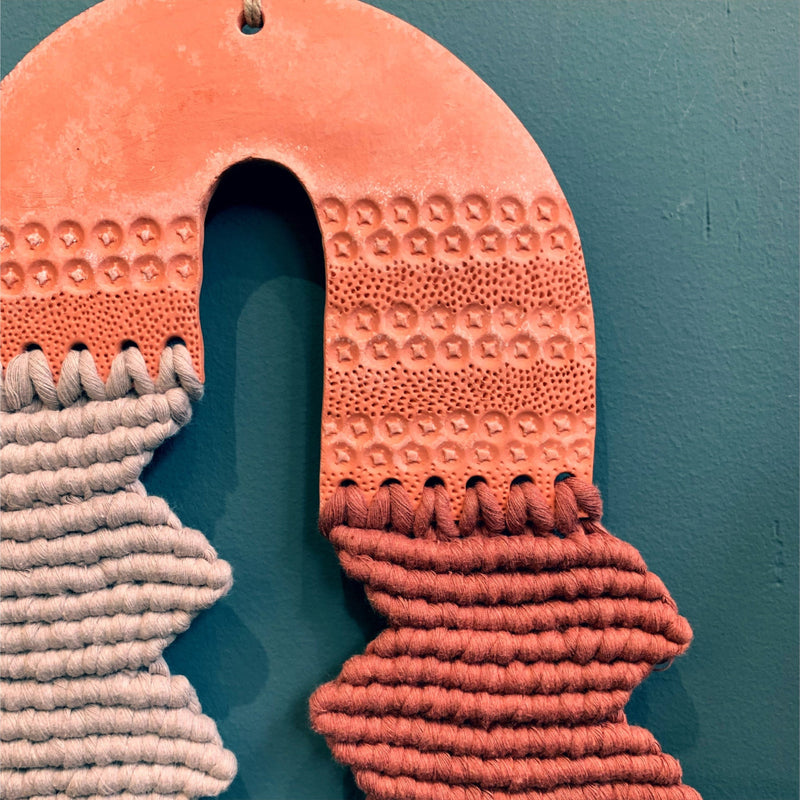 Detail of a clay U shaped patterned element with a knotted zig zag pattern in grey and rust against a teal background