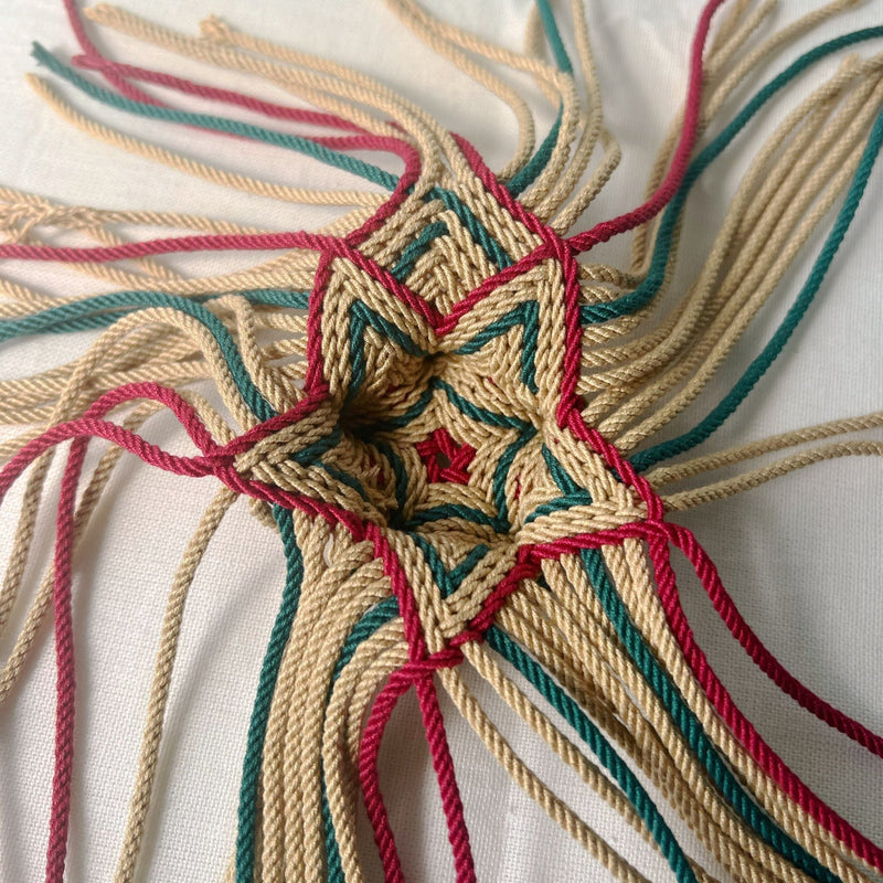 Star-shaped ply-split braiding 3D design with red, green, and beige threads on a white background