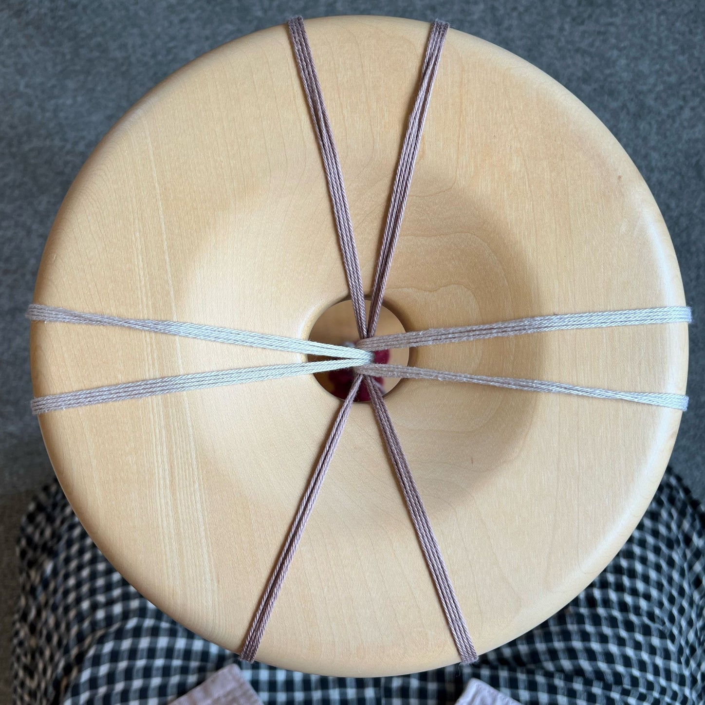 The surface of a wooden Madurai with 8 groups of yarns centered out from the point of braid on a grey and checked background.