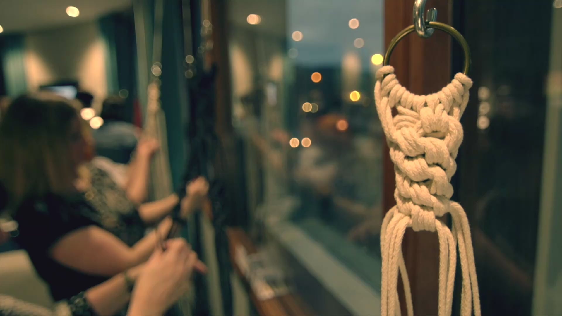 Load video: A group of focused people making plant hangers at an ASTRL Fibres workshop in a warmly lit room during the evening.
